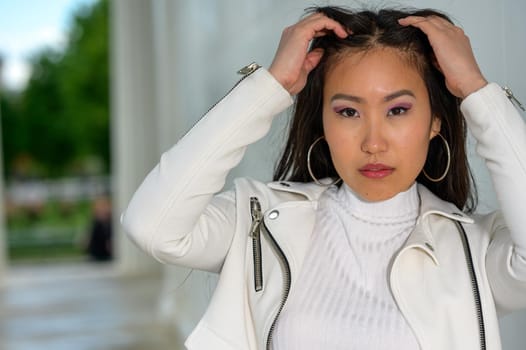 A young pretty Mongolian woman with a white leather jacket
in an urban park.