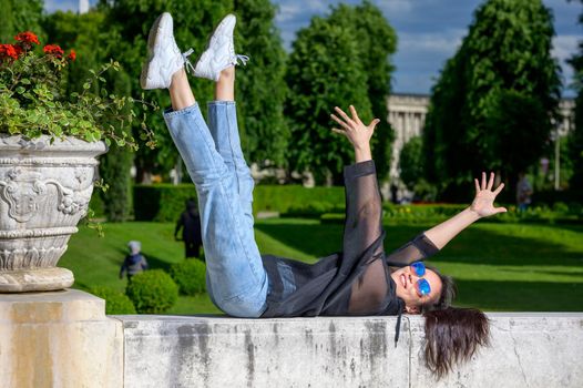 A very pretty young Mongolian girl is having fun in a park and enjoying the sun. She is lying on her back on a wall.