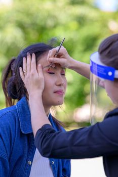 A pretty Mongolian woman is being made up in a park by a make-up artist for a photo shoot.