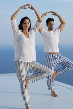 young couple practicing yoga at sunset in modern home terace with ocean and sunset in background