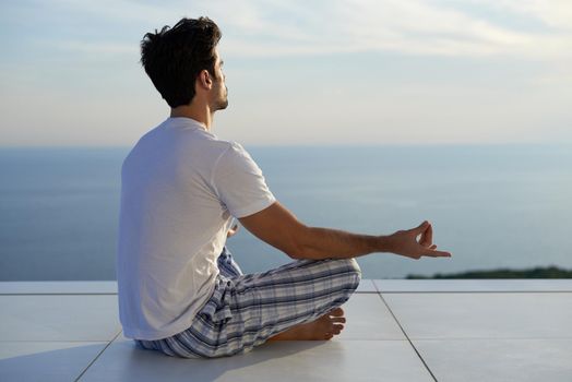 handsome young man practicing yoga on in modern home terace with ocean and sunset in background