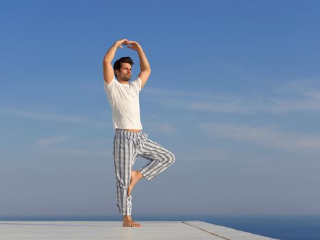 handsome young man practicing yoga on in modern home terace with ocean and sunset in background