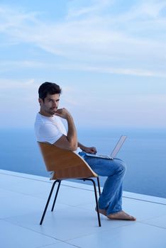 handsome young man relaxing and working on laptop computer at home balcony while looking sunset