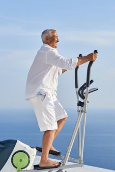 healthy senior man working out on gym treadmill machine at modern home terace with ocean view