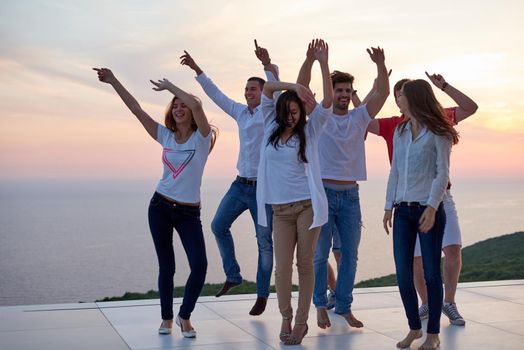 group of happy young people dancing and have fun on party in modern home bacony with sunset and ocean in background