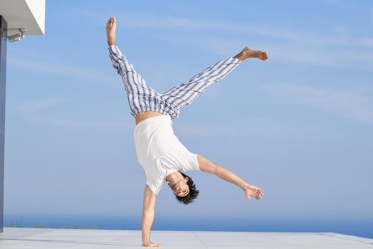 handsome young man practicing yoga on in modern home terace with ocean and sunset in background