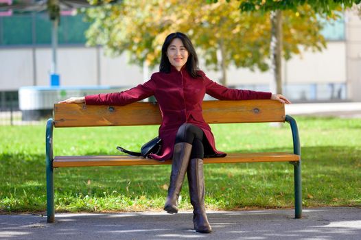 Beautiful chinese woman with long black hair on a sunny autumn day in the city, sitting on a bench in the warm autumn sun,