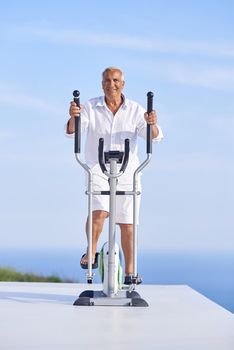 healthy senior man working out on gym treadmill machine at modern home terace with ocean view