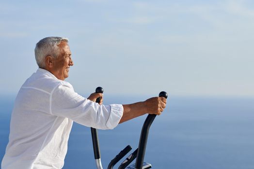 healthy senior man working out on gym treadmill machine at modern home terace with ocean view