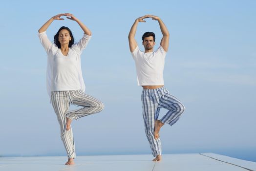 young couple practicing yoga at sunset in modern home terace with ocean and sunset in background