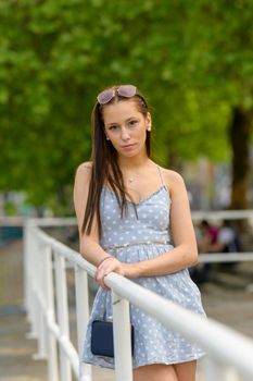 A portrait of a pretty young woman, taken in the summer in a city, leaning against a railing on a nearby river.