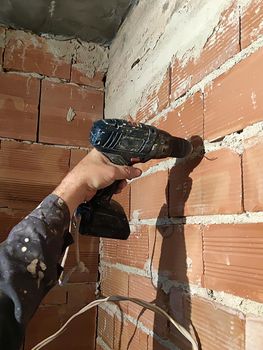 male hand with drill drills brick wall, renovation