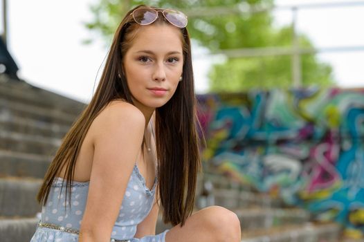 A portrait of a pretty young woman taken in the summertime in a city sitting on a staircase next to a river.