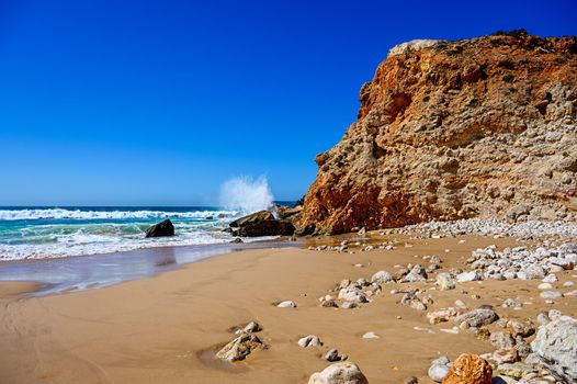 A beach with high rough cliffs at the Algarve in Portugal with some powerful waves.