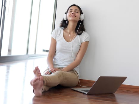 beautiful young woman relax and work on laptop computer modern  home office while listening musin on white headphones