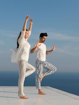 young couple practicing yoga at sunset in modern home terace with ocean and sunset in background