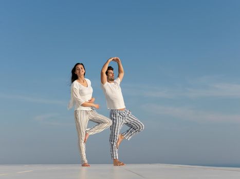 young couple practicing yoga at sunset in modern home terace with ocean and sunset in background