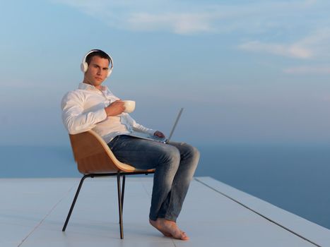 handsome young man relaxing and working on laptop computer at home balcony while looking sunset