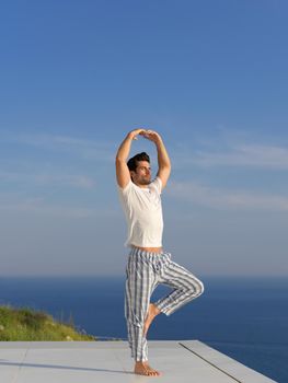 handsome young man practicing yoga on in modern home terace with ocean and sunset in background