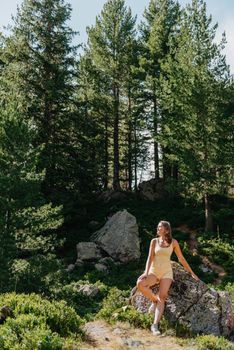 Young woman tourist sitting on the mountain peak and beautiful mountains. Landscape with sporty girl, green forest, hills , sky, lake. Travel and tourism. Hipster girl in the mountains. Stylish woman in checkered shirt sitting on stones in forest. Wanderlust concept. Hiking and travelling in summer. mysterious wood. Beautiful nature