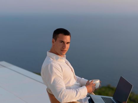 handsome young man relaxing and working on laptop computer at home balcony while looking sunset