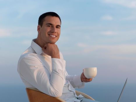 handsome young man relaxing and working on laptop computer at home balcony while looking sunset