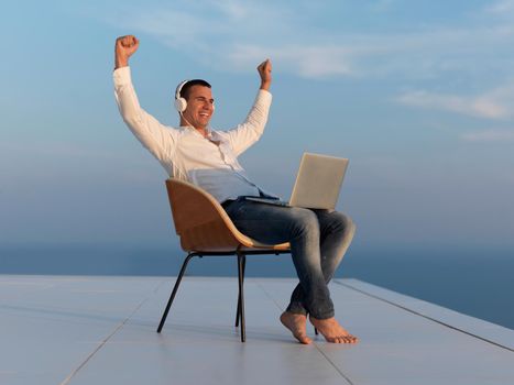 handsome young man relaxing and working on laptop computer at home balcony while looking sunset