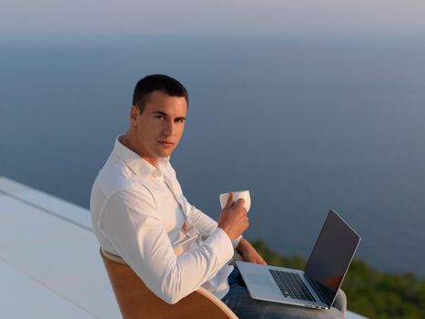 handsome young man relaxing and working on laptop computer at home balcony while looking sunset