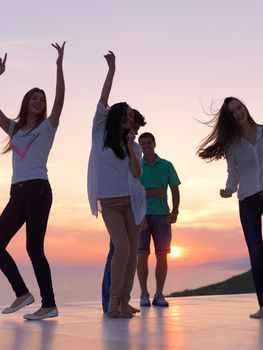 group of happy young people dancing and have fun on party in modern home bacony with sunset and ocean in background