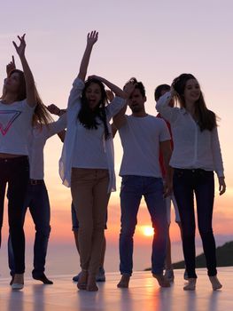 group of happy young people dancing and have fun on party in modern home bacony with sunset and ocean in background