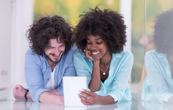 Happy young multiethnic couple lying on floor having fun using Digital Tablet