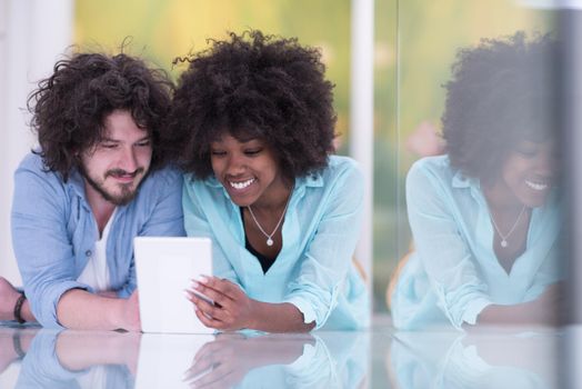 Happy young multiethnic couple lying on floor having fun using Digital Tablet