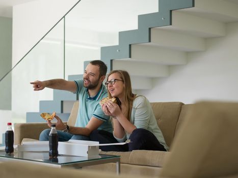 young handsome couple cheerfully spending time while eating pizza in their luxury home villa