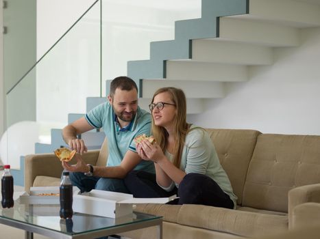 young handsome couple cheerfully spending time while eating pizza in their luxury home villa