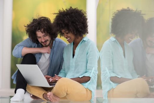 Young beautiful multiethnic couple using a laptop and doing shopping online while sitting on the floor