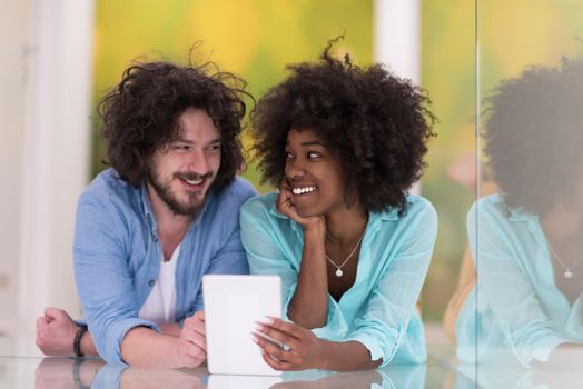 Happy young multiethnic couple lying on floor having fun using Digital Tablet