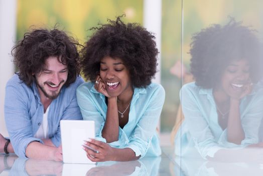 Happy young multiethnic couple lying on floor having fun using Digital Tablet