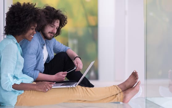 Young beautiful multiethnic couple using a laptop and doing shopping online while sitting on the floor