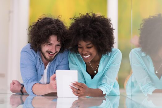 Happy young multiethnic couple lying on floor having fun using Digital Tablet