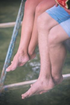 group of  people sitting at wooden bridge over the river with a focus on hanging legs