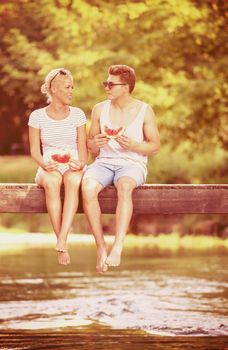 couple in love enjoying watermelon while sitting on the wooden bridge over the river in beautiful nature