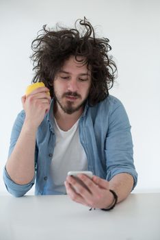 Handsome casual young man eating apple and using a mobile phone at  home