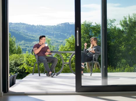 young beautiful handsome couple enjoying morning coffee and breakfast in front of their luxury home villa