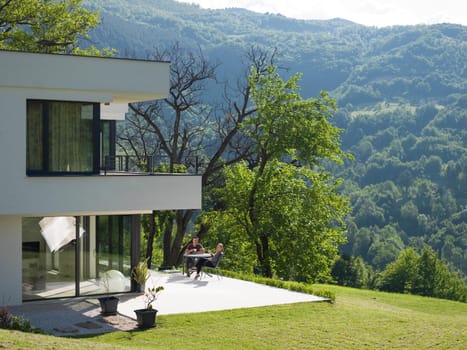 young beautiful handsome couple enjoying morning coffee and breakfast in front of their luxury home villa