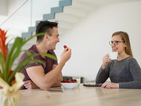 young beautiful handsome couple enjoying morning coffee and strawberries in their luxurious home villa