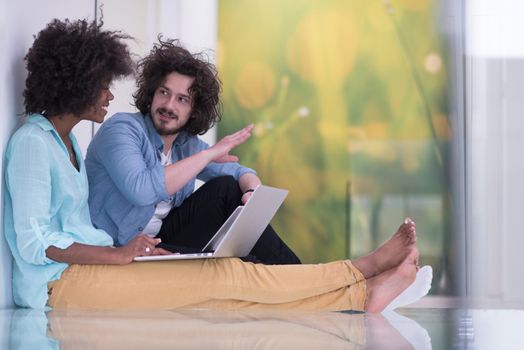 Young beautiful multiethnic couple using a laptop and doing shopping online while sitting on the floor