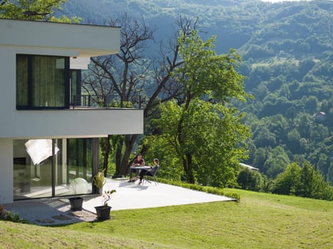 young beautiful handsome couple enjoying morning coffee and breakfast in front of their luxury home villa