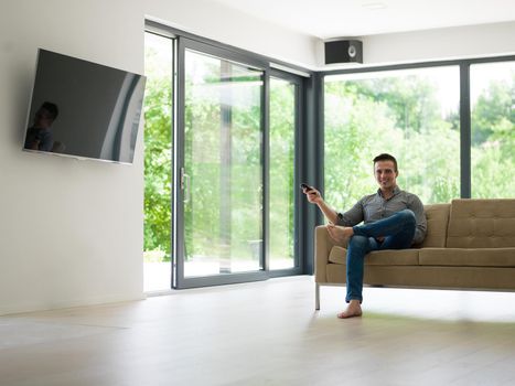 young handsome man enjoying free time watching television in his luxury home villa