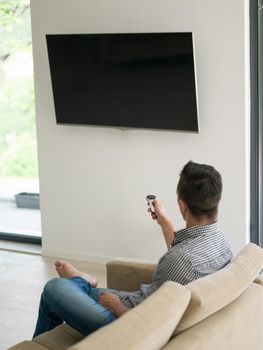 young handsome man enjoying free time watching television in his luxury home villa