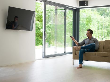 young handsome man enjoying free time watching television in his luxury home villa